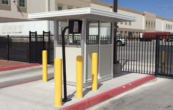 Small security booth with yellow bollards outside a gated area in an industrial complex.